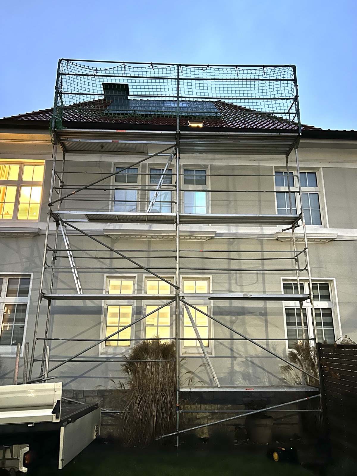 Fassadengerüst mit Dachfangnetz an einem Mehrfamilienhaus in der Dämmerung